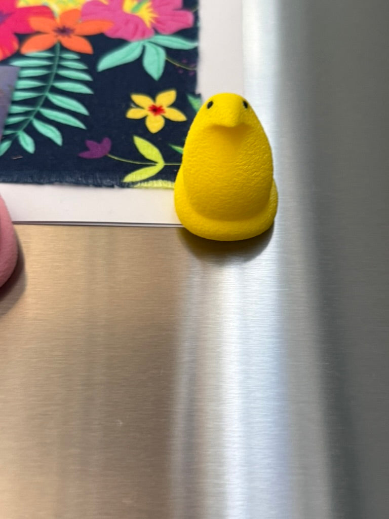 Yellow duck-shaped object on a metallic surface with a floral mat in the background