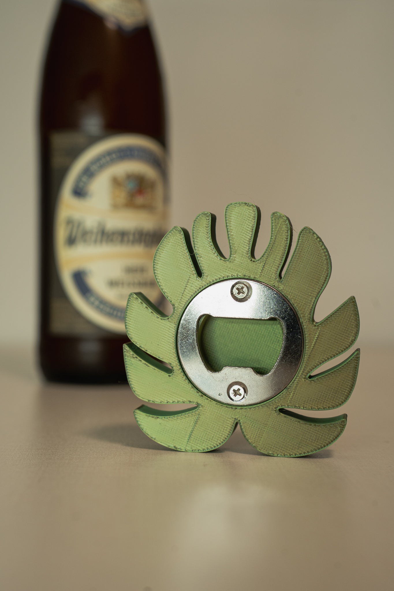 Green bottle opener with leaf design in front of a beer bottle