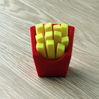 A red container-shaped item filled with yellow rectangular pieces, photographed on a light wood-grain surface.