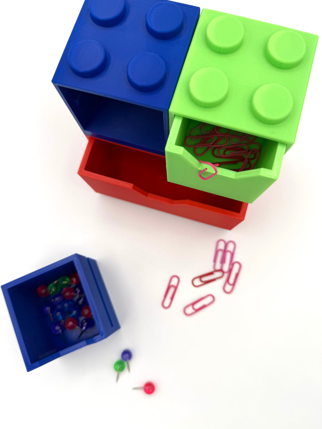 Colorful storage boxes resembling LEGO bricks with paper clips and pins on a white background