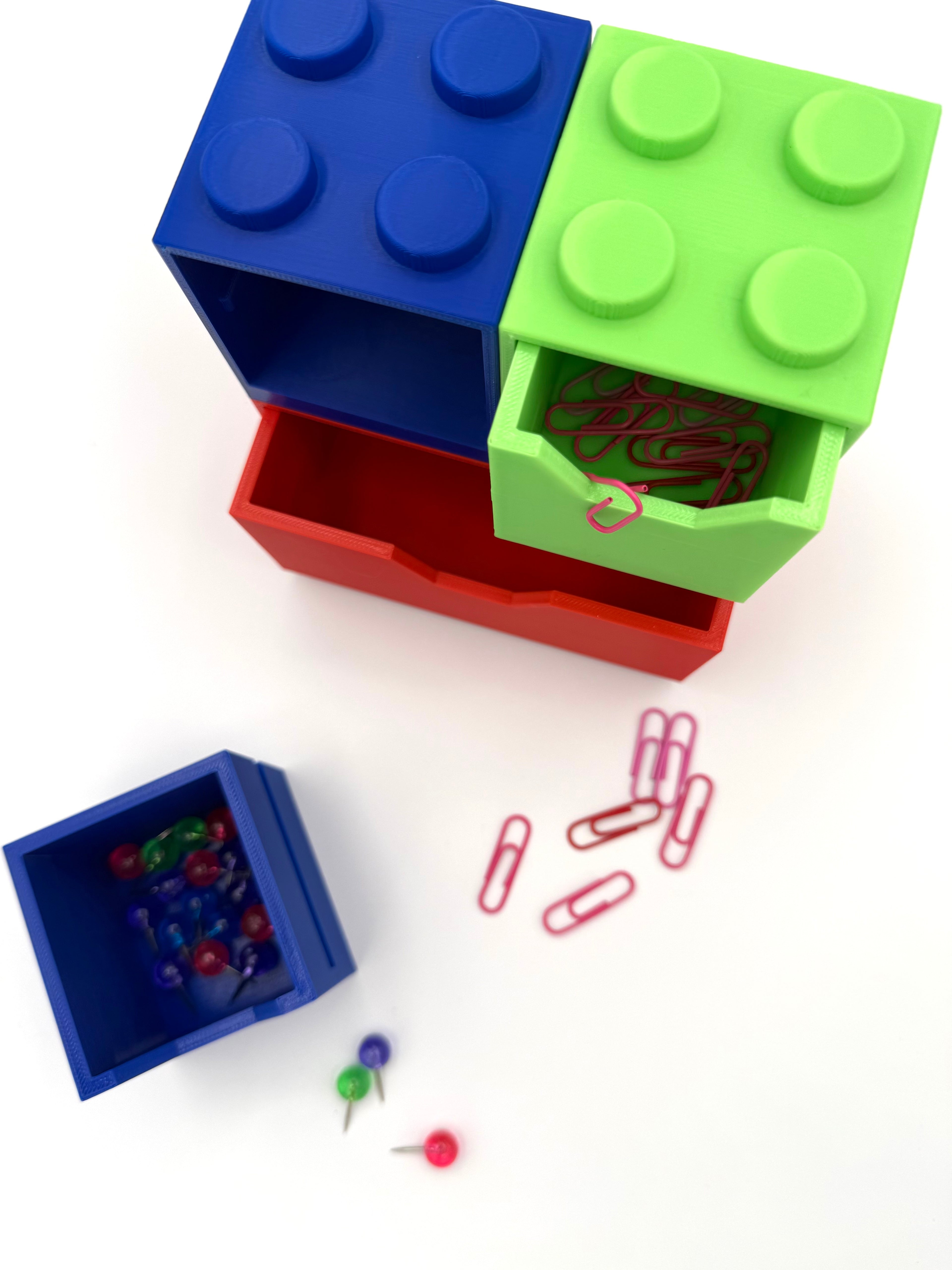 Colorful storage boxes resembling LEGO bricks with paper clips and pins on a white background
