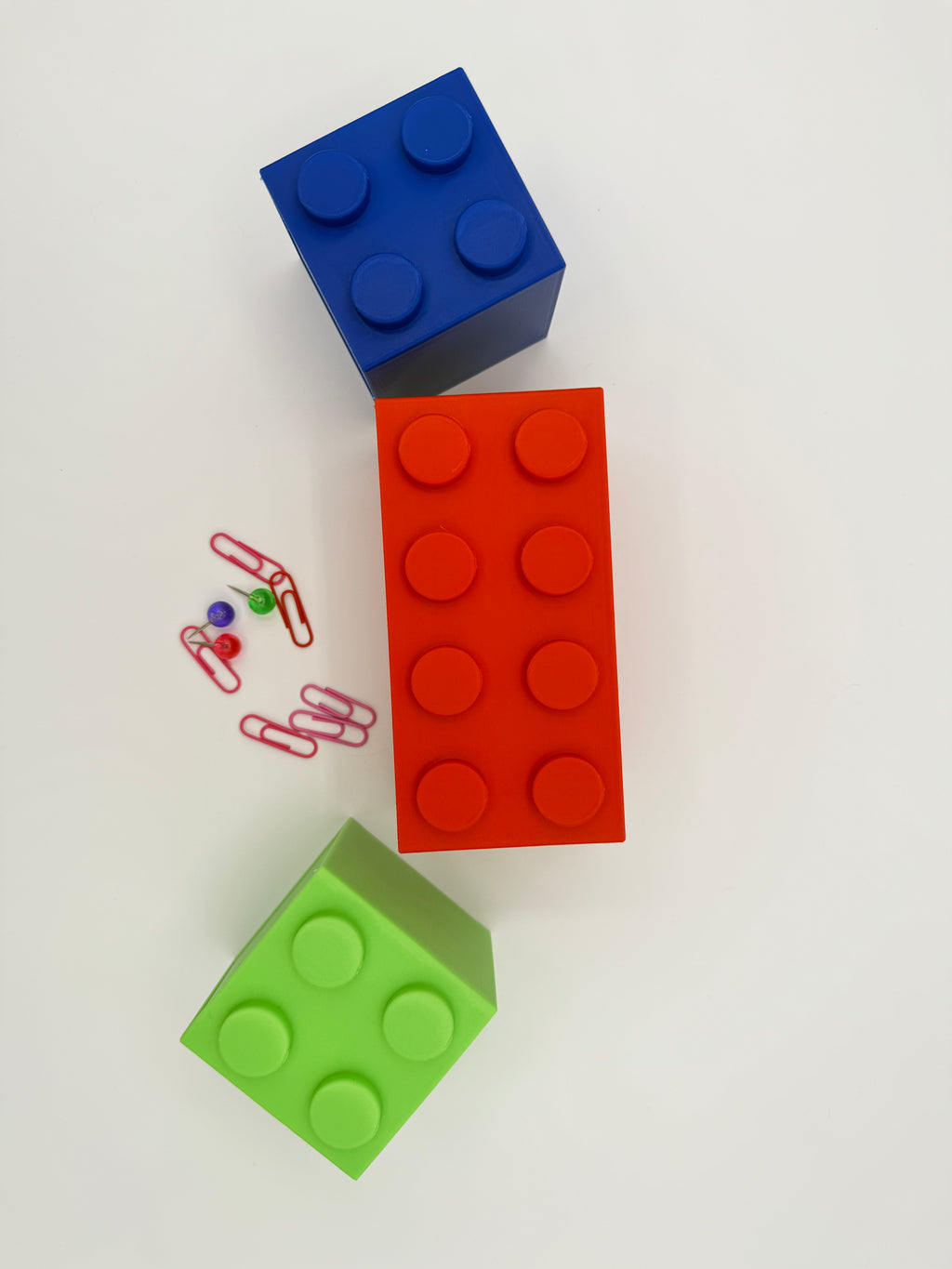 Three colorful building blocks (blue, red, green) on a white background with small colorful objects.