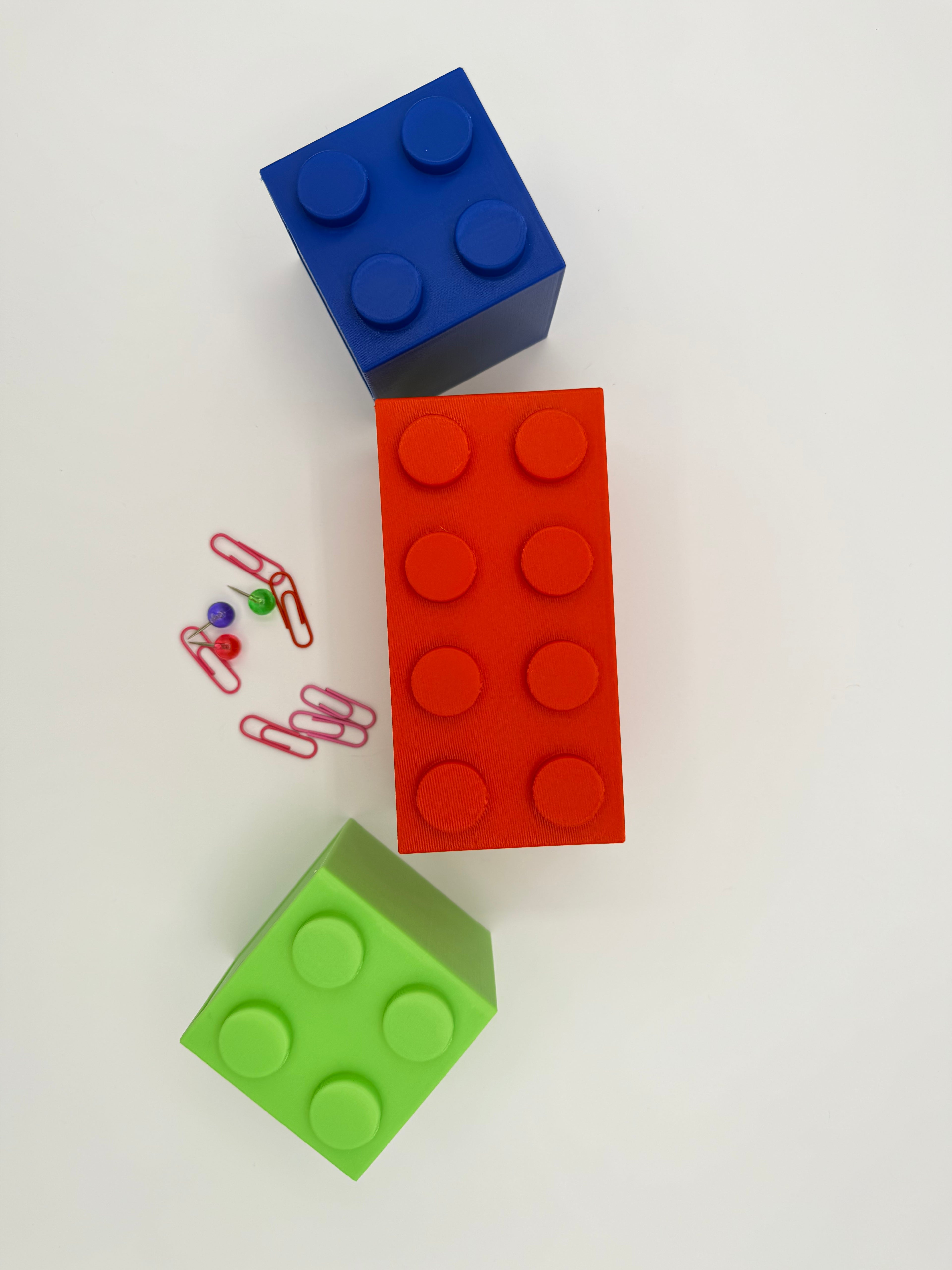 Three colorful building blocks (blue, red, green) on a white background with small colorful objects.