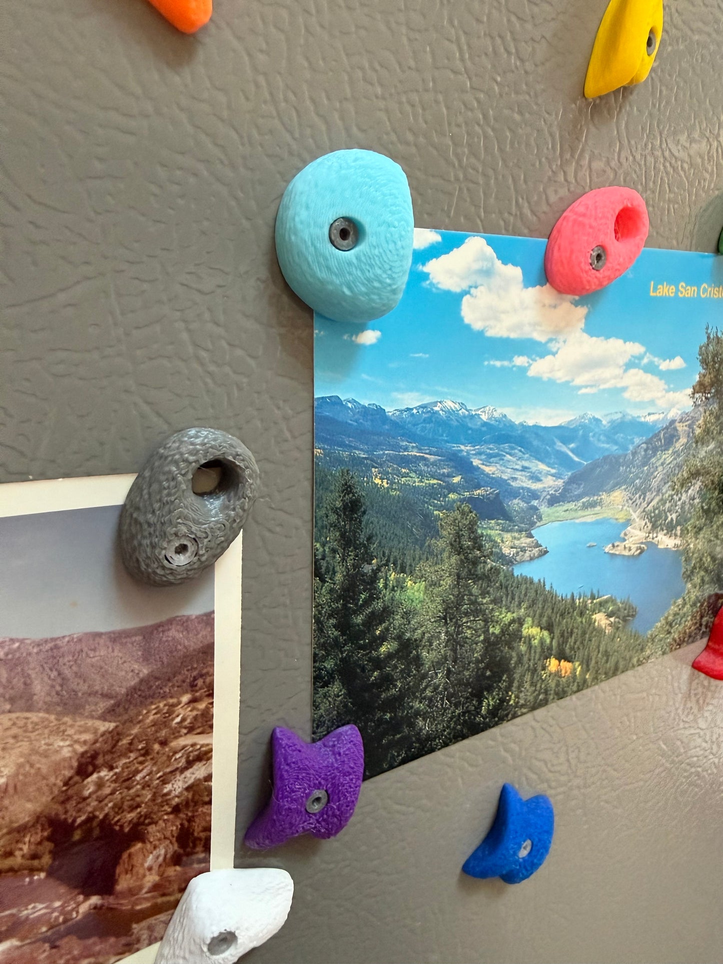 Colorful magnetic rock bouldering photo holders on a refrigerator with scenic photos attached.