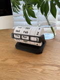 Calendar roll on a wooden surface with a plant in the background