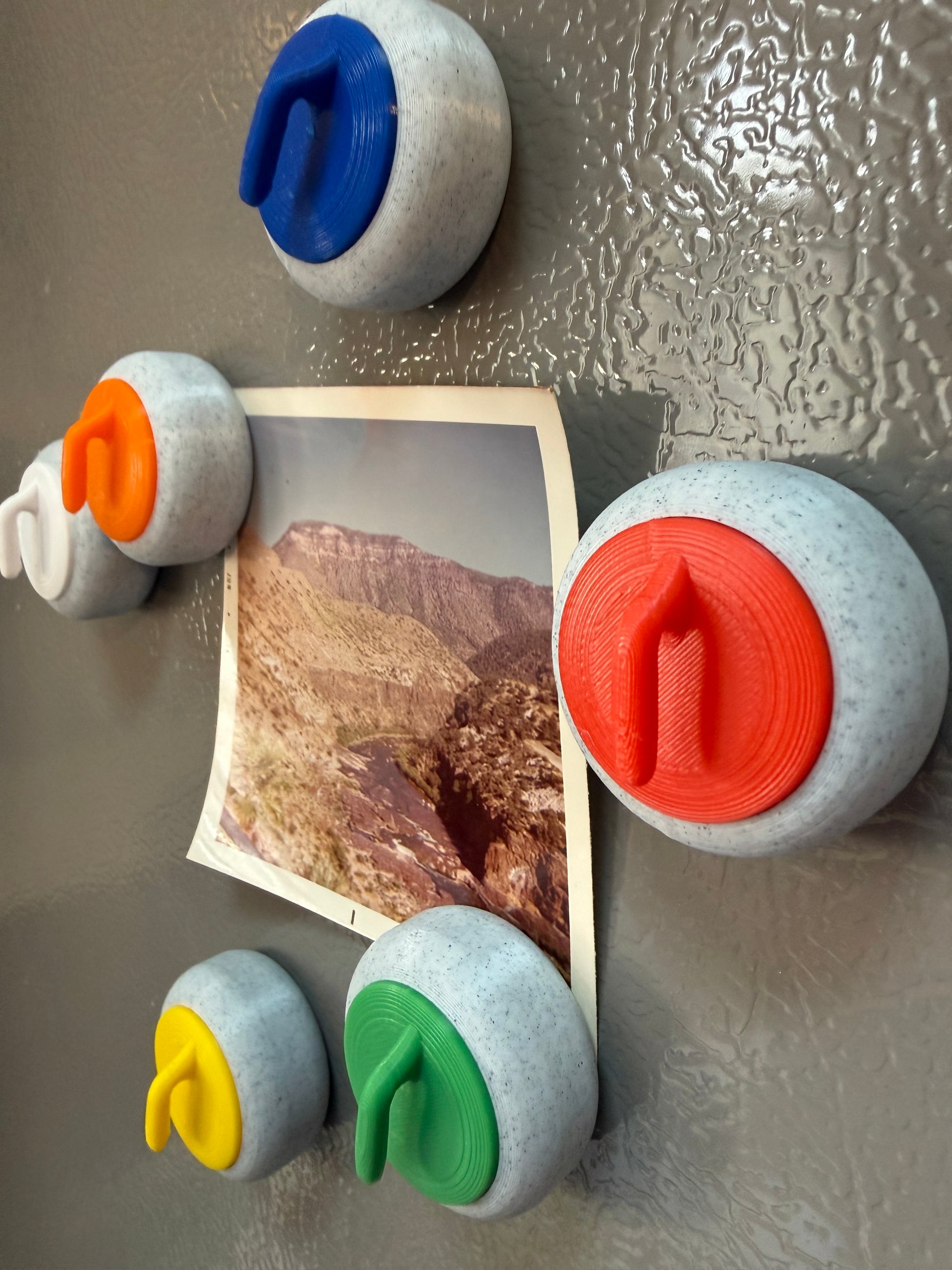 Colorful curling stones on a refrigerator with a photo of a mountain landscape.