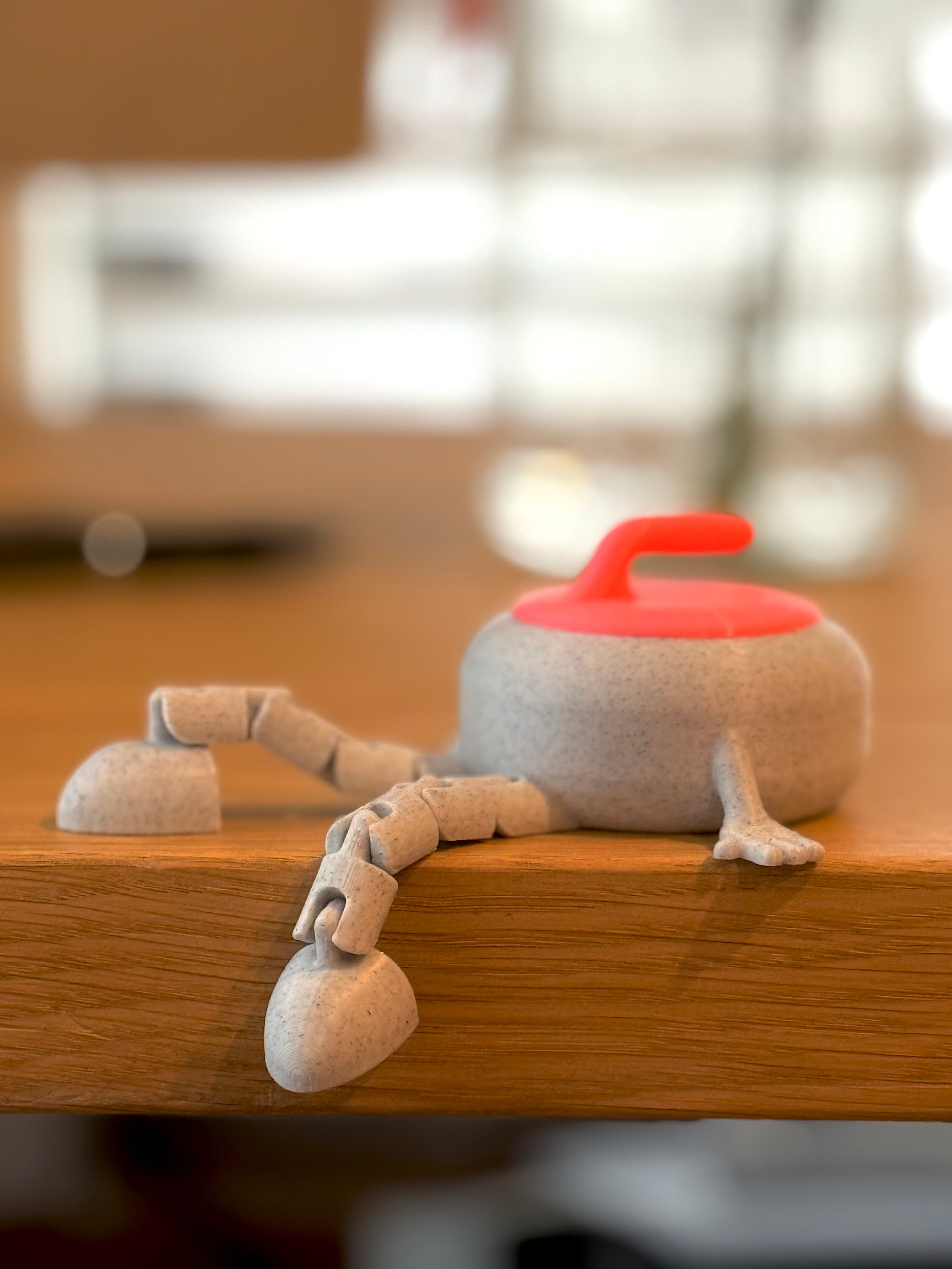 Small gray curling stone buddy with a pink lid on a wooden surface