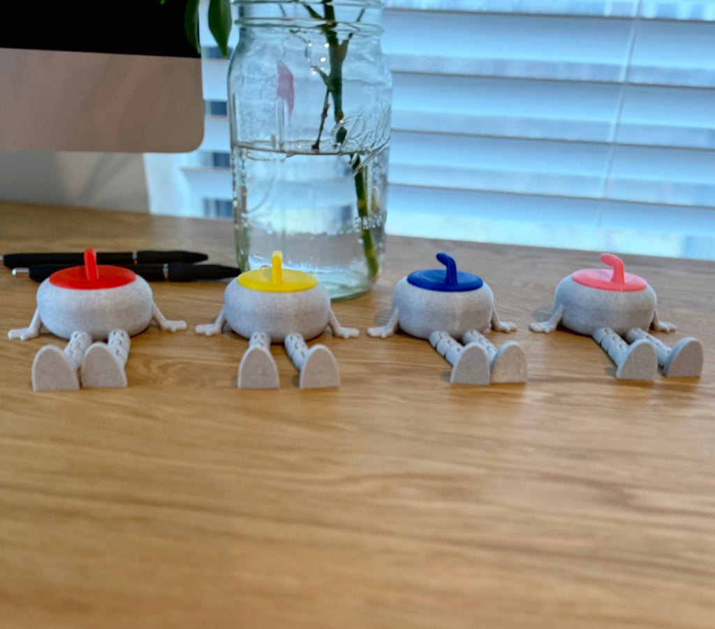 Four small flexi curling stone buddies with colored heads on a wooden surface.
